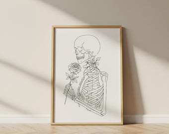 May include: A framed art print with a minimalist line drawing of a skeleton holding a rose. The artwork is in black and white, with the skeleton's rib cage and skull clearly defined. The frame is a light wood colour.