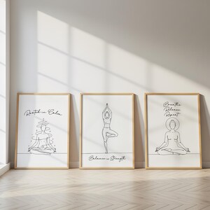 May include: Three framed art prints with line drawings of yoga poses. The prints have a white background and are in wooden frames. The first print says "Rooted in Calm", the second says "Balance is Strength", and the third says "Breathe Release Repeat".