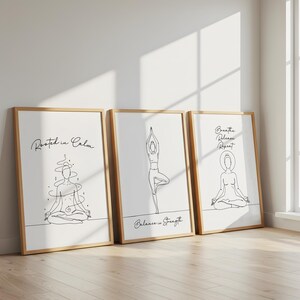May include: Three framed art prints with line drawings of yoga poses. The prints have a white background and wooden frames. Text on the prints reads "Rooted in Calm", "Balance is Strength", and "Breathe Release Repeat".