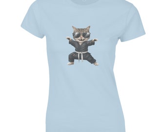 Op de afbeelding: Een lichtblauw t-shirt met een cartoon afbeelding van een kat met een zonnebril en een zwart karatepak. De kat staat in een vechtpose.
