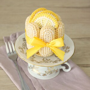 Puede incluir: Un pastel de lim&oacute;n tejido a crochet con una cinta amarilla sobre una taza de t&eacute; y un platillo blancos.