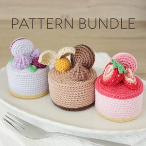 May include: Three crocheted cakes with various toppings sit on a white plate. The cakes are in shades of purple, brown, and pink, with details like a macaron, berries, and a strawberry. The text "PATTERN BUNDLE" is at the top.