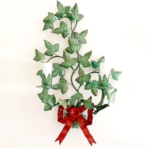 Peut inclure: Une applique murale en métal vert en forme de vigne feuillue avec deux bougeoirs et un nœud rouge en bas.