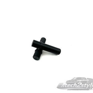 May include: Two black cylindrical objects are positioned in a crossed arrangement against a white background. The objects appear to be made of a solid, matte material. The image is well-lit, highlighting the simple shapes.