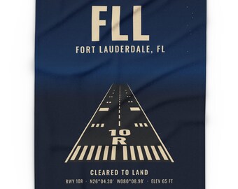 May include: A dark blue blanket featuring a graphic of an airport runway with the text FLL FORT LAUDERDALE, FL, 10 R, CLEARED TO LAND, RWY 10R, N26°04.30' W080°08.98', and ELEV 65 FT printed in a light cream color on the fabric.