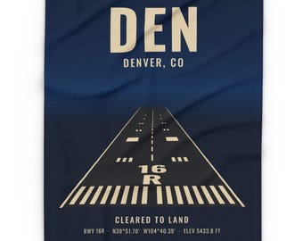 May include: A dark blue blanket featuring a graphic of an airport runway with the text DEN DENVER, CO, 16 R, CLEARED TO LAND, RWY 16R, N39°51.70' W104°40.39', and ELEV 5433.8 FT printed in a light cream color.