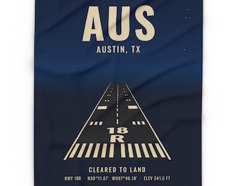 May include: A dark blue blanket featuring a graphic of an airport runway with the text AUS AUSTIN, TX at the top and CLEARED TO LAND RWY 18R N30°11.67' W097°40.19' ELEV 541.5 FT at the bottom, centered around the runway markings.