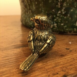 Pu&ograve; includere: Una piccola statuetta di uccello dorata con piume dettagliate. L'uccello &egrave; rivolto a sinistra e ha le ali ripiegate.