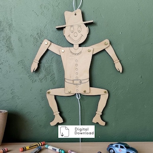 Puede incluir: Una marioneta articulada de madera clara que representa una figura con sombrero, camisa con cinturón y botas. Las extremidades están unidas con cierres metálicos y cuelga un cordel blanco. El texto dice Digital Download.