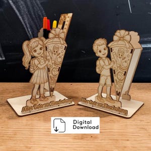 Könnte beinhalten: Zwei Holzdekorationen in Form von Schultüten, eine mit einem Mädchen und die andere mit einem Jungen, die jeweils eine Tüte mit Illustrationen zum Thema Schule halten. Die Tüten haben eine Schleife oben und den Text "Alles Gute zur, Einschulung" auf der Basis.