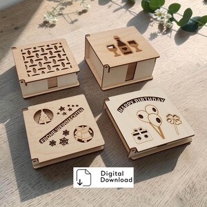 Könnte beinhalten: Vier quadratische, helle Holzschachteln mit Laserschnitt-Motiven. Eine zeigt ein geometrisches Muster, eine andere eine Sektflasche mit Gläsern, eine weitere einen Weihnachtsbaum, Glocken und den Text "FROHE WEIHNACHTEN", sowie eine mit Luftballons, einem Geschenk und "HAPPY BIRTHDAY".
