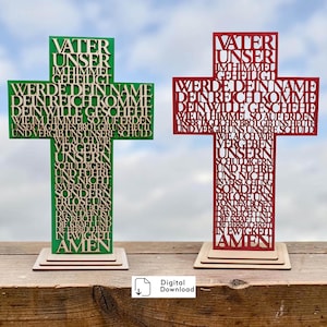 May include: Two cross-shaped decorative items, one green and one red, each featuring the German Lord's Prayer cut out in a bold, sans-serif font. Both crosses are mounted on tiered, light-colored wooden bases, displaying the text Vater Unser.