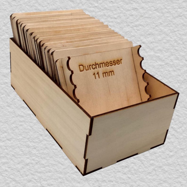 May include: A light-colored wooden storage box containing a series of thin, rectangular wooden dividers or cards. The front-most card features the laser-engraved text "Durchmesser 11 mm" and has scalloped edges on both the left and right sides.