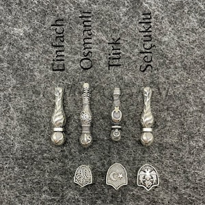 May include: Silver-toned metal pendants and charms. The pendants have ornate designs, and the charms feature emblems. The word "Einfach" is above one pendant, "Osmanlı" above another, "T&uuml;rk" above a third, and "Sel&ccedil;uklu" above the last.