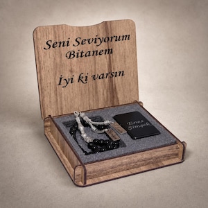 Könnte beinhalten: Eine Holzschatulle mit offenem Deckel und der Gravur "Seni Seviyorum Bitanem" sowie "Iyi ki varsın". Im Inneren befinden sich schwarze Gebetsperlen mit silbernen Akzenten und eine schwarze, rechteckige Metallplatte mit der Gravur "Enes Şimşek".