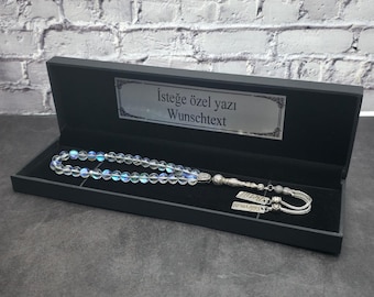 May include: A string of iridescent prayer beads with silver accents and two rectangular silver charms engraved with the names Betül and Süleyman, presented in a black rectangular box with a plaque reading İsteğe özel yazı Wunschtext.