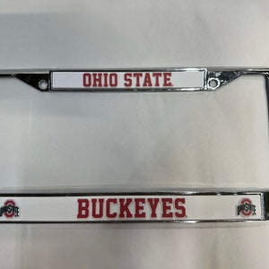 May include: A chrome license plate frame with a white background and red lettering. The top of the frame says "OHIO STATE" and the bottom says "BUCKEYES".