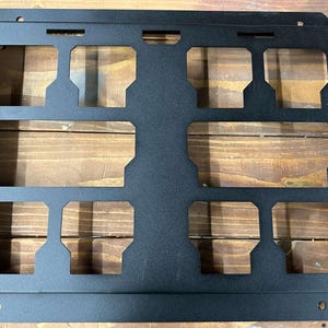 May include: Black metal wall mount with nine rectangular cutouts. The mount is designed to hold items like tools or other small objects.