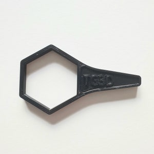 May include: A black plastic wrench with a hexagonal opening and the text "TG3D" printed on the handle.