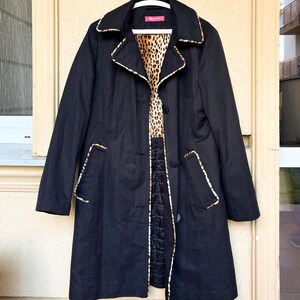 May include: A black trench coat featuring a notched collar, long sleeves, and a button-front closure. The coat is accented with leopard print trim along the collar, lapels, and pocket edges, and includes a leopard print lining on the upper interior.