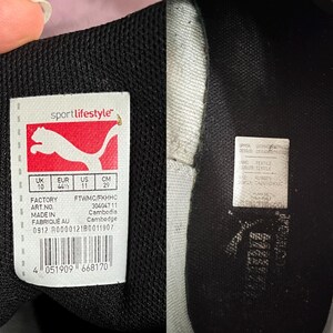 Pu&ograve; includere: Una scarpa Puma bianca e nera con un'etichetta nera sul lato. L'etichetta presenta il logo Puma e il testo "sportlifestyle". L'etichetta include anche informazioni sulle dimensioni in UK, EUR, US e CM. L'etichetta include anche la fabbrica, il numero d'articolo e il paese d'origine. La scarpa ha una suola in gomma nera.