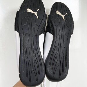 Pu&ograve; includere: Un paio di scarpe da ginnastica Puma bianche e nere con suola testurizzata. Le scarpe hanno una tomaia in pelle bianca e una suola in gomma nera.