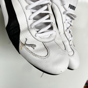 Pu&ograve; includere: Un paio di scarpe da ginnastica Puma in pelle bianca con dettagli neri e un logo Puma sul lato. Le scarpe hanno lacci e una suola in gomma bianca.