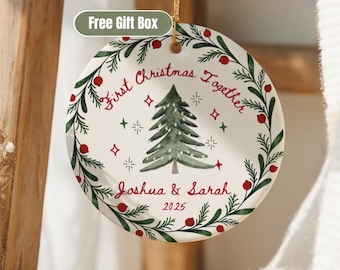 May include: A round Christmas ornament with a watercolor Christmas tree design. The ornament has a green wreath with red berries and the text "First Christmas Together" and the names "Joshua & Sarah" with the year 2025.