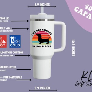 May include: White insulated tumbler with a handle, featuring a dachshund silhouette against a sunset design and the text "I've Got Friends in Low Places." It has a 40 oz capacity, is 10.5 inches tall, and 3.9 inches wide. The tumbler is made of stainless steel.