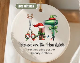 May include: A white ceramic ornament with a gold string, featuring a festive design for hairstylists. It includes scissors with reindeer antlers, a comb with a Santa hat, and a green hair dryer. The text reads "Blessed are the Hairstylists".