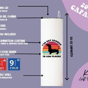 May include: A white 20 oz stainless steel tumbler with a dachshund silhouette and the text "I've Got Friends In Low Places." Features include a sliding lid, straw, and double-wall vacuum insulation. Keeps drinks hot for 3 hours and cold for 9 hours.