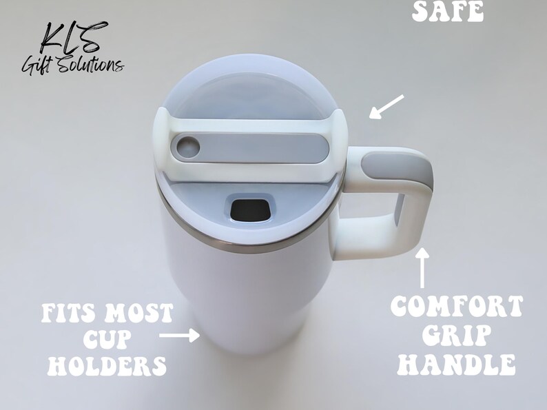 May include: White travel mug with a gray lid and handle. Features include a comfort grip handle, and the text "FITS MOST CUP HOLDERS" and "SAFE". The mug is designed for easy use and portability.
