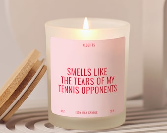 Puede incluir: Vela de cera de soja en vaso de vidrio esmerilado con mecha encendida y etiqueta rosa claro que dice KLSGIFTS, SMELLS LIKE THE TEARS OF MY TENNIS OPPONENTS, 8OZ y 35 H. Una tapa circular de bambú con sello de silicona blanco descansa al lado.