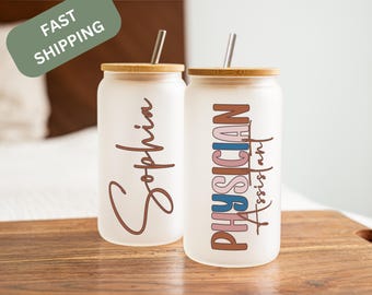 May include: Two frosted glass tumblers with bamboo lids and straws. One tumbler has the name "Sophia" written in brown script. The other tumbler has the text "Physician Assistant" written in colorful letters.