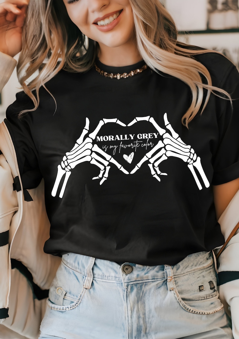 K&ouml;nnte beinhalten: Schwarzes T-Shirt mit einem wei&szlig;en Skelett-Hand-Design, das eine Herzform bildet. Der Text "Morally Grey is my favorite color" befindet sich im Herzen.