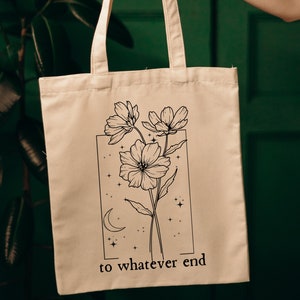 May include: A white canvas tote bag with black line art of flowers and stars. The text "to whatever end" is printed on the bag.