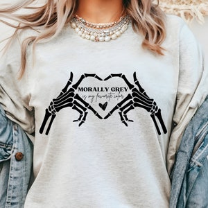 K&ouml;nnte beinhalten: Ein hellgraues Sweatshirt mit einer schwarzen Grafik aus zwei Skeletth&auml;nden, die eine Herzform bilden. Der Text "MORALLY GREY is my favorite color" befindet sich im Herzen.