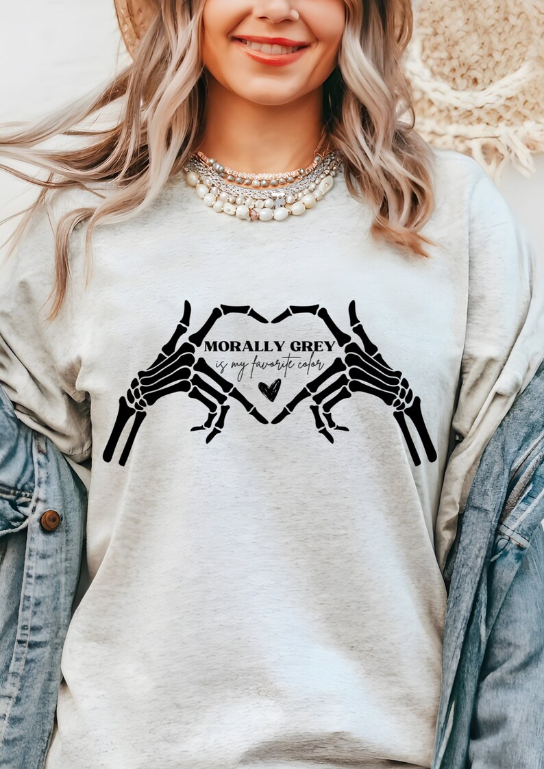 K&ouml;nnte beinhalten: Ein hellgraues Sweatshirt mit einer schwarzen Grafik aus zwei Skeletth&auml;nden, die eine Herzform bilden. Der Text "MORALLY GREY is my favorite color" befindet sich im Herzen.