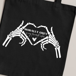 K&ouml;nnte beinhalten: Schwarze Einkaufstasche mit wei&szlig;en Skeletth&auml;nden, die eine Herzform bilden. Der Text im Herzen lautet "Morally Grey is my favorite color".