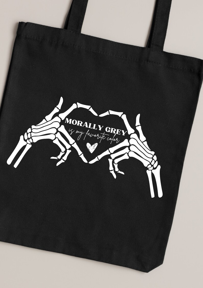 K&ouml;nnte beinhalten: Schwarze Einkaufstasche mit wei&szlig;en Skeletth&auml;nden, die eine Herzform bilden. Der Text im Herzen lautet "Morally Grey is my favorite color".