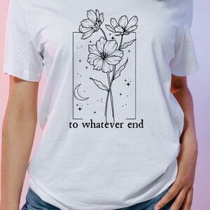 May include: A white t-shirt with a black line drawing of flowers, a crescent moon, and stars inside a rectangle. The text "to whatever end" is below the rectangle.