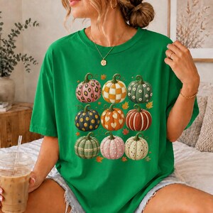 May include: A bright green short-sleeve t-shirt featuring a graphic print of nine pumpkins in a three-by-three grid. Each pumpkin displays a unique pattern, including leopard print, checkered, polka dots, hearts, stripes, and floral motifs.