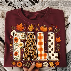 May include: A maroon crewneck t-shirt featuring the word FALL in large block letters. Each letter has a unique pattern: floral, leopard print, orange and white buffalo plaid, and white with brown polka dots, surrounded by autumn leaves and pumpkins.