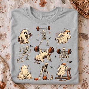 Pode incluir: Uma t-shirt cinza mesclado com uma estampa gráfica de vários fantasmas e esqueletos a fazer exercício. As ilustrações incluem fantasmas a levantar halteres, a correr e a meditar, juntamente com esqueletos a levantar pesos e a fazer agachamentos.