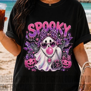 Può includere: Una t-shirt nera con la grafica di un fantasma bianco che indossa un fiocco leopardato, occhiali da sole rosa a forma di cuore e una collana di perline. Il fantasma soffia una bolla rosa, tiene una borsa con la scritta Trick or Treat ed è circondato da zucche viola, pipistrelli, ragnatele e la parola SPOOKY in lettere viola gocciolanti.