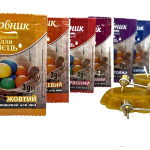 May include: Assortment of food coloring packets for dyeing Easter eggs. The packets are labeled with the colors: yellow, red, brown, blue, green. Each packet contains 3 grams of food coloring. The image also shows a small candle and two wooden sticks with metal tips.