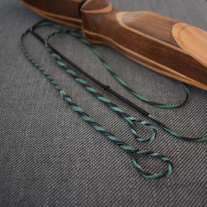 Könnte beinhalten: Nahaufnahme einer schwarzen und grünen Bogensehne mit einem Holzbogen im Hintergrund.