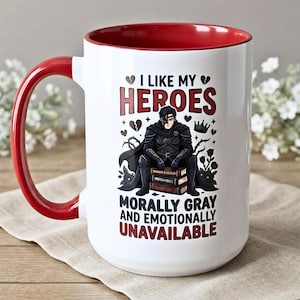 Puede incluir: Taza de cerámica blanca con interior y asa rojos. La taza presenta el texto "I LIKE MY HEROES" y "MORALLY GRAY AND EMOTIONALLY UNAVAILABLE" con una ilustración de un personaje sentado sobre libros.