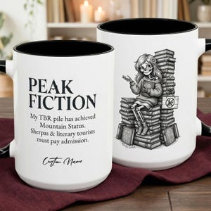 Puede incluir: Dos tazas de cerámica blancas con interiores y asas negras. Una taza tiene el texto "PEAK FICTION" y una cita sobre libros. La otra taza presenta un esqueleto leyendo sobre una pila de libros.