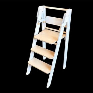 Könnte beinhalten: Ein weißer Holztreppenhocker mit integriertem Stuhl und Sicherheitsgeländer. Der Hocker hat vier Stufen und ist für Kinder konzipiert.